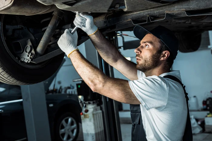 bearded auto mechanic in cap repairing automobile in car service